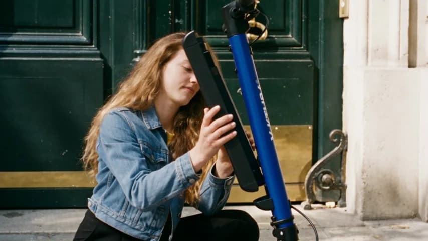 Une personne avec sa trottinette électrique V-KTURA bleue devant une porte cochère parisienne